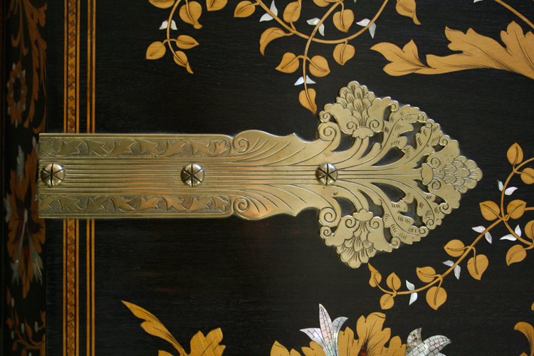 Large, ornate brass hinges secure the piano lid. The stamped hinges continue the themes of foliage and flowers found in the cabinet inlay