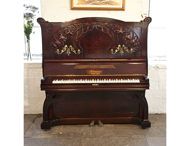 An Art Nouveau Knauss Upright Piano For Sale with a Mahogany Case Carved with Flowers and Flowing Tendrils. Cabinet features Ornate Brass Candlesticks and Handles