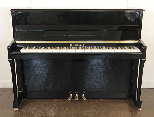 A Steinmayer upright piano with a black case and brass fittings.