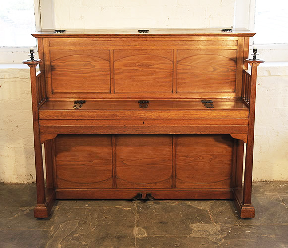A 1903, Arts and Crafts style, Bluthner upright piano with a polished, oak case. Cabinet features large, sculptural candlesticks and ornate, iron hinges.