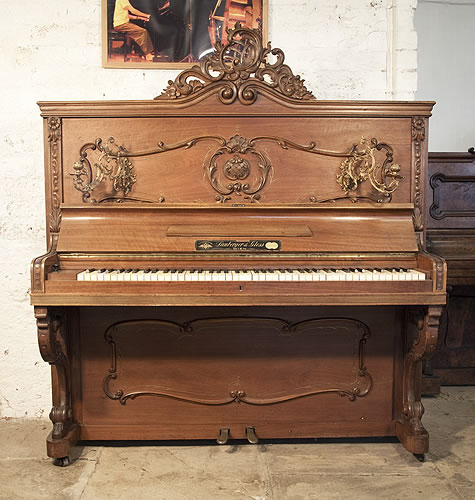 Lamberger & Gloss upright piano with a Rococo style, mahogany case with ornate brass candlesticks and scroll foot legs. Cabinet features scrolling acanthus, shells and rocaille detail and an ornate, asymmetrical pediment.