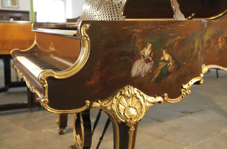 Steinway Model B ornately carved, piano cheek with gilt accents. The hand-painted scene features two ladies sitting outdoors discussing a book and gathering flowers in a basket.