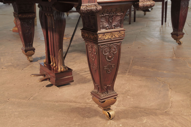 The three piano legs are heavily carved, yet appear understated due to minimal use of gilted filigree banding. Each leg is a tapered, four-sided baluster shape, carved with sunflowers and foliage