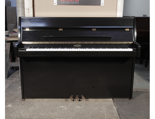Pre-owned, 1995, Kemble upright piano with a black polished case and brass fittings. Piano has an eighty-eight note keyboard and two pedals.