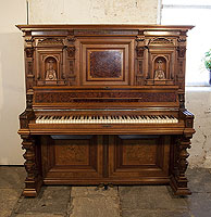 A German upright piano with a Neoclassical style walnut case and cup and cover legs. Cabinet features ornately carved pilasters in high reief and copper sconces in a sea monster design.