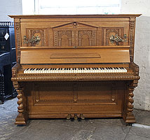 A Helmholz upright piano for sale with a Romanesque style, oak case and barley twist legs. Cabinet features a front panel ornately carved with rounded arches and grotesque heads on piano cheeks