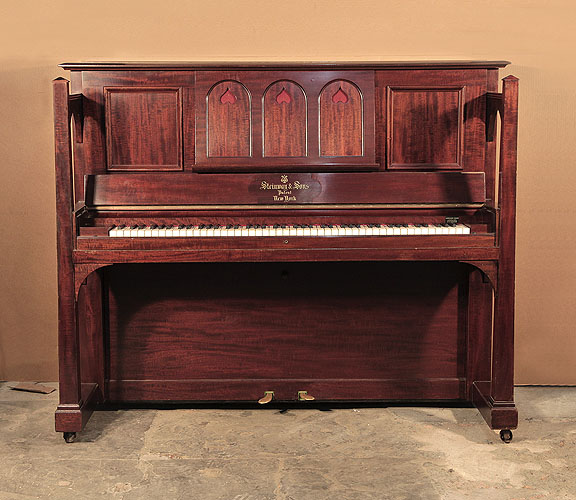Arts and Crafts style,  1905, Steinway  upright piano for sale with a figured, mahogany case and large sculptural legs. Cabinet features a music desk in a three arche design with cut-out inverted hearts backed with red felt