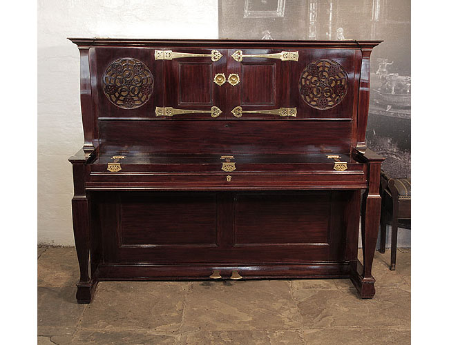 An 1897, Arts and Crafts style, Bechstein upright piano with a rosewood case, fretwork panels and ornate brass hinges in a stylised floral design. Unique design by Walter Cave, executed by C. Bechstein and exhibited by Maple & Co