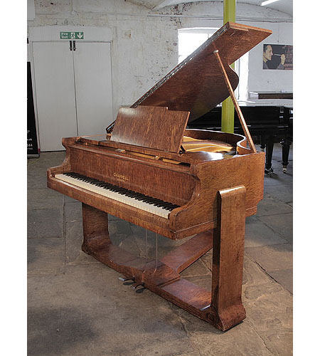 A 1936, Art Deco style, Chappell baby grand piano for sale with a quilted maple case. Cabinet features sculptural piano legs that integrate into the piano cabinet and are attached with a cross stretcher.