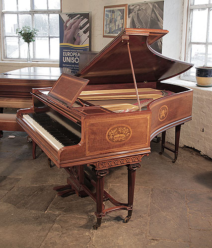 An 1894, Broadwood grand piano with a fiddleback mahogany case and tapered fluted legs attached with a cross stretcher. Cabinet inlaid with oval panels featuring musical instruments, foliage and flowers and satinwood crossbanding and stringing accents 