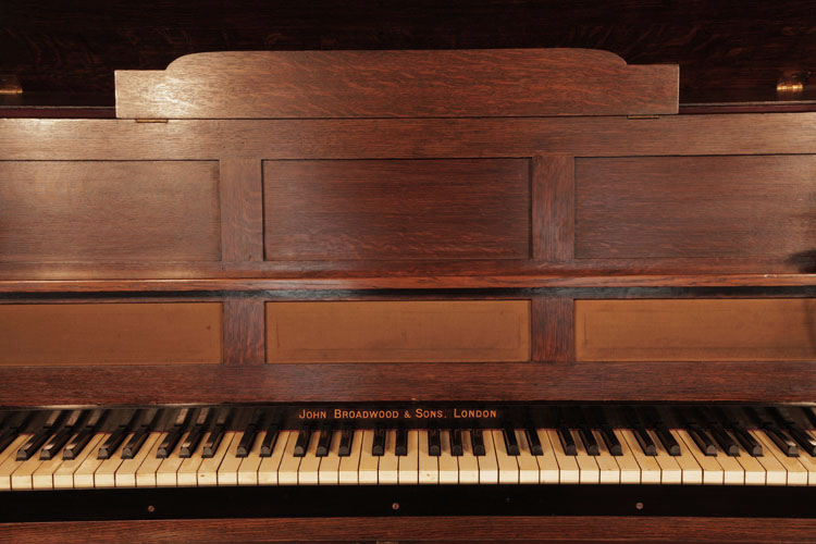 Broadwood music desk is incorporated into the piano cabinet with a hinged scalopped top. Cabinet features three openwork panels backed in fabric.