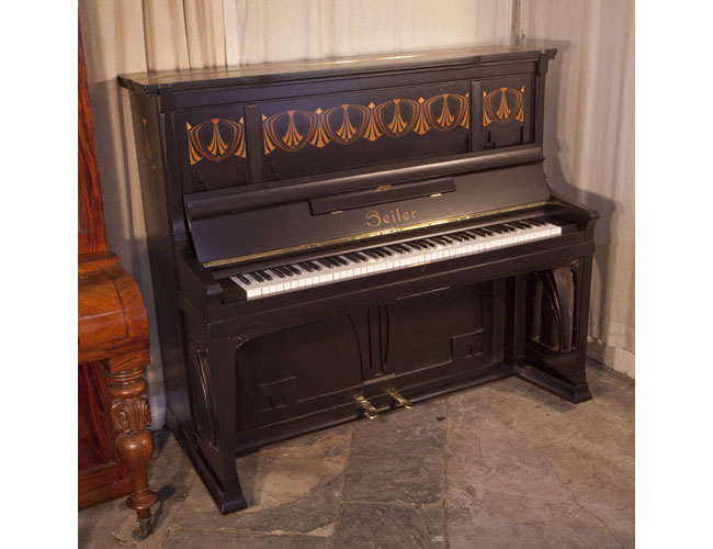 A 1906, Seiler upright piano with a Jugenstil, black satin case. Cabinet panels inlaid with repeated, stylised fans within bold geometric, angular forms