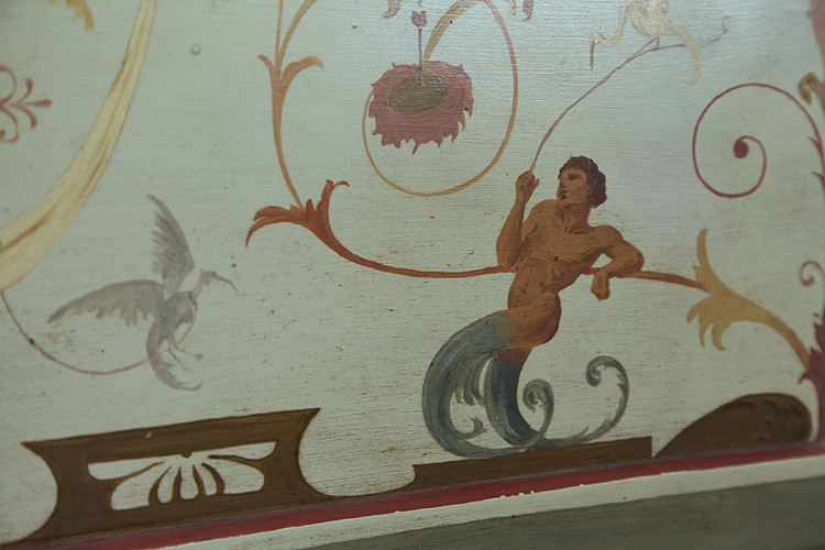 Hand-painted detail of a reclining male figure with birds and arabesques.