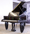 The Golden Age of Pianos Exhibition. A Steinway model B grand piano with an ebonised case. Case features three tiered mouldings at base. Music desk has a geometric filigree design. Piano has three barrel legs each carved with figures playing musical instruments and floral relief detail. Designed by Oskar Kaufmann